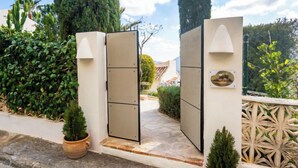A gated entrance with a stone pathway leading to a building, surrounded by lush greenery and potted plants. - Petite Fleur by Interhome (Jávea)