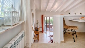 A bright, open-plan living space with a large window, a dining area with a wicker chair, and a white shelf with small plants. - Petite Fleur by Interhome (Jávea)