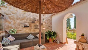 A cozy outdoor seating area with a stone wall, a wicker sofa, a thatched umbrella, and a potted plant. - Petite Fleur by Interhome (Jávea)