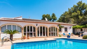 A swimming pool with a tiled edge, a palm tree, and a building with arched windows and a tiled roof. - Villa Mariposa by Interhome (Jávea)