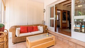 A cozy living area with a wicker sofa, a glass coffee table, and a sliding glass door leading to a kitchen. - Villa Mariposa by Interhome (Jávea)