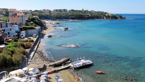 Una località balneare con spiaggia, imbarcazioni ed edifici lungo la costa.