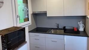 Une cuisine compacte dotée d’un four encastré, d’un évier et d  ’une fenêtre donnant sur un espace verdoyant.