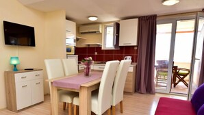 Un espace de vie compact comprenant un coin repas, une kitchenette et un téléviseur fixé au mur.