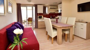 Un espace de vie compact comprenant un coin repas, une kitchenette et un canapé rouge agrémenté de coussins violets.