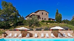 Un bâtiment en pierre doté d’une piscine et de chaises longues.