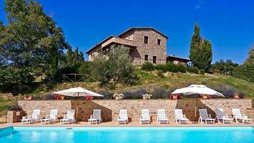 Ein Steinhaus mit Pool und Liegestühlen.