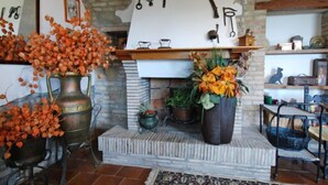Een rustiek interieur met een stenen openhaard, decoratieve vazen en diverse gereedschappen aan de muur.