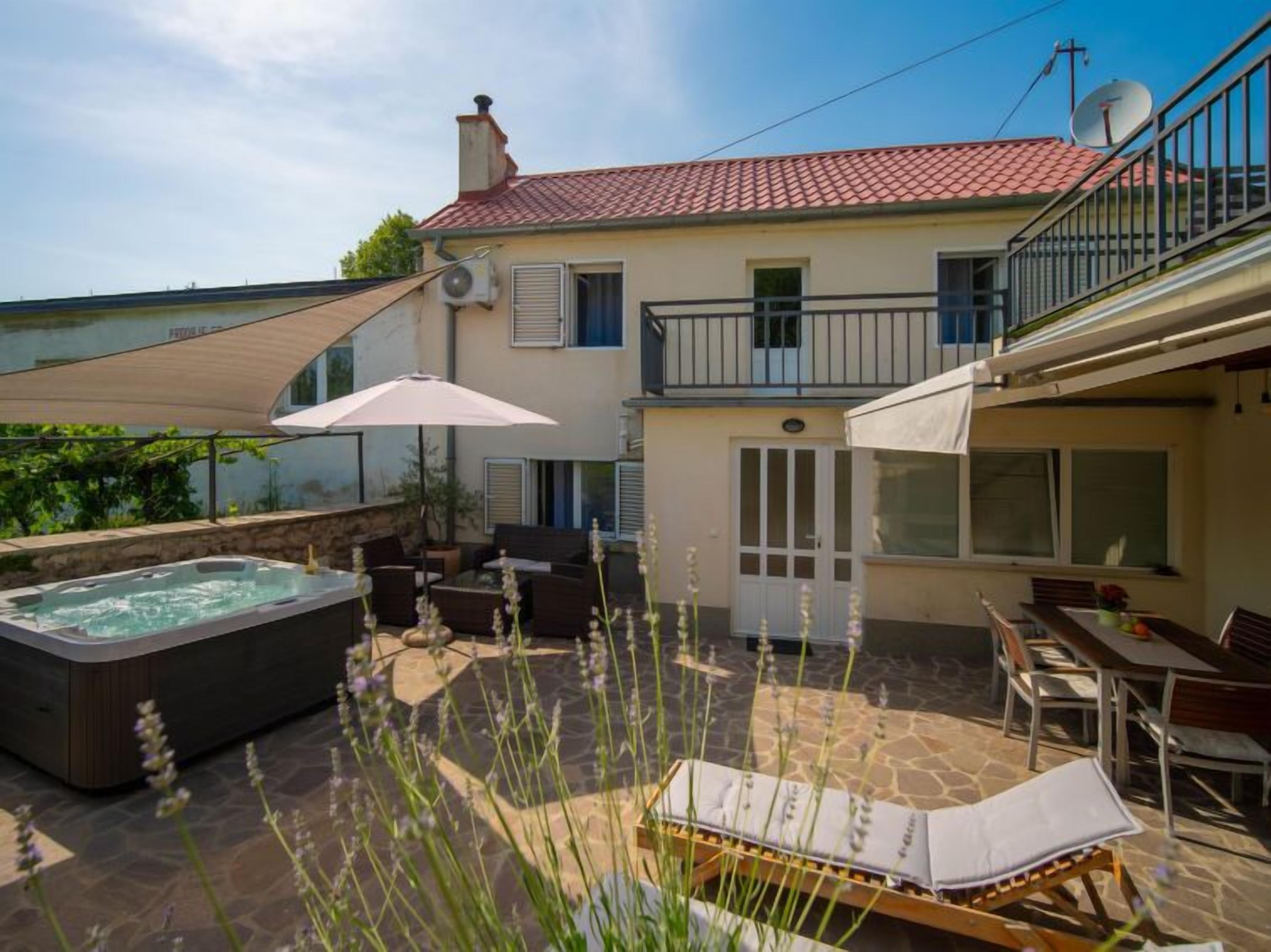 Un patio con jacuzzi, mobiliario exterior y vista a una casa con tejado rojo.