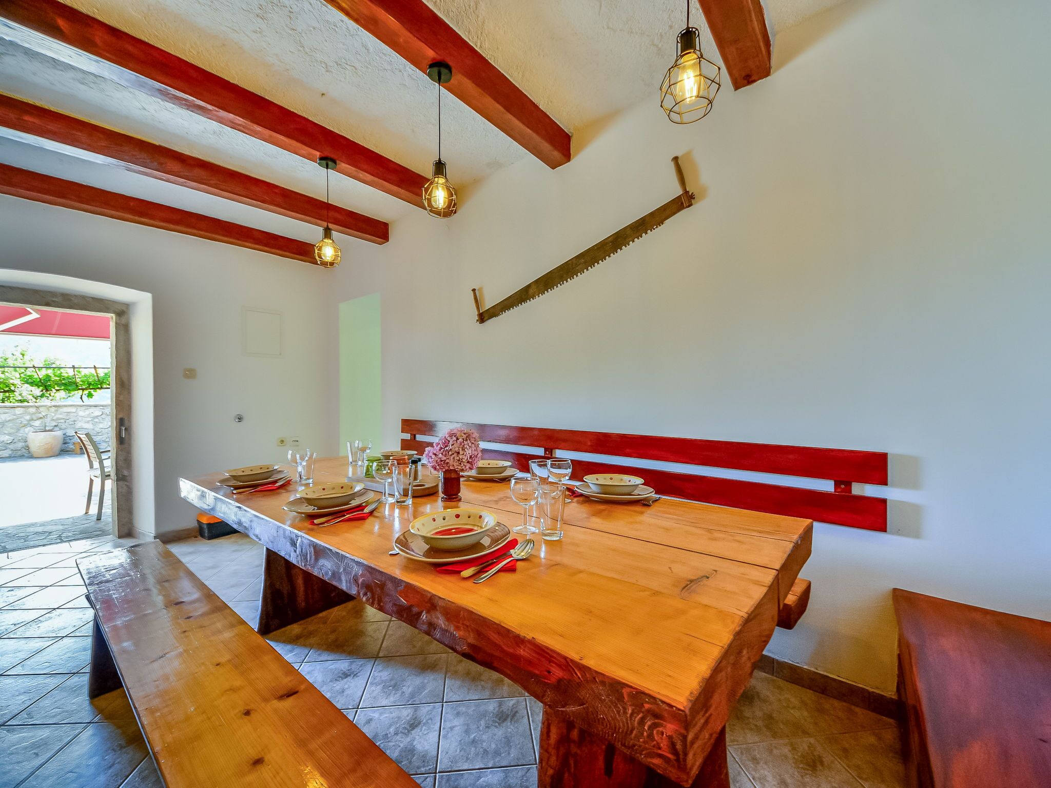 A dining area with a wooden table set for four, benches, and hanging pendant lights.