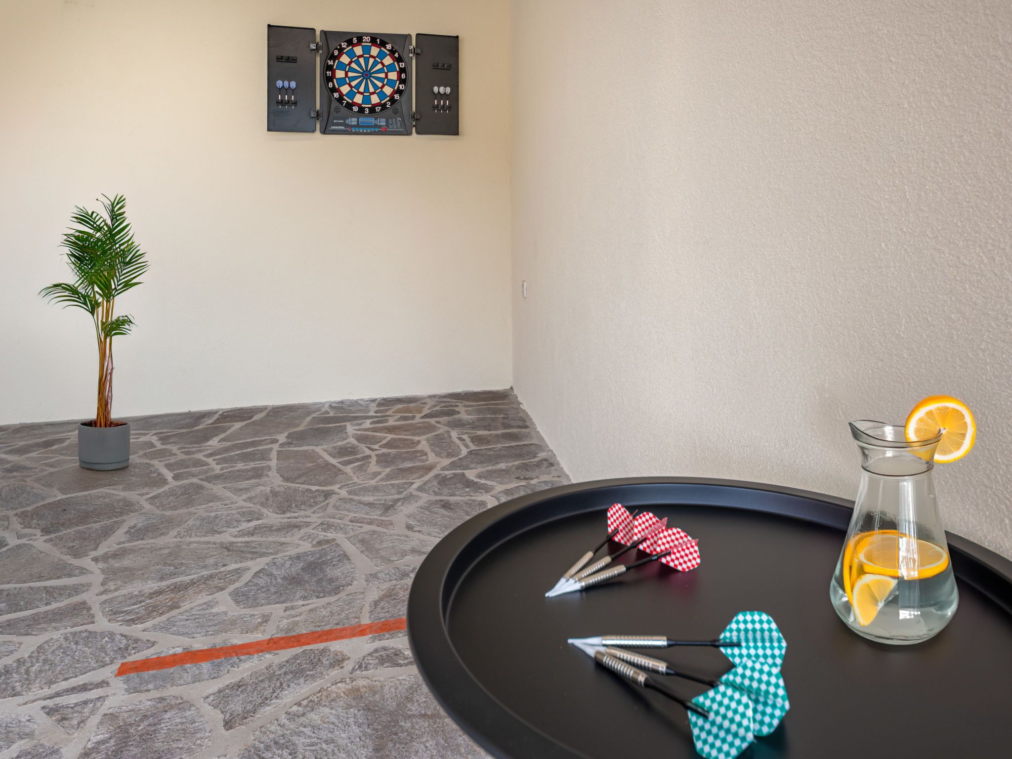 A dartboard, a potted plant, and a pitcher with a lemon slice on a table.