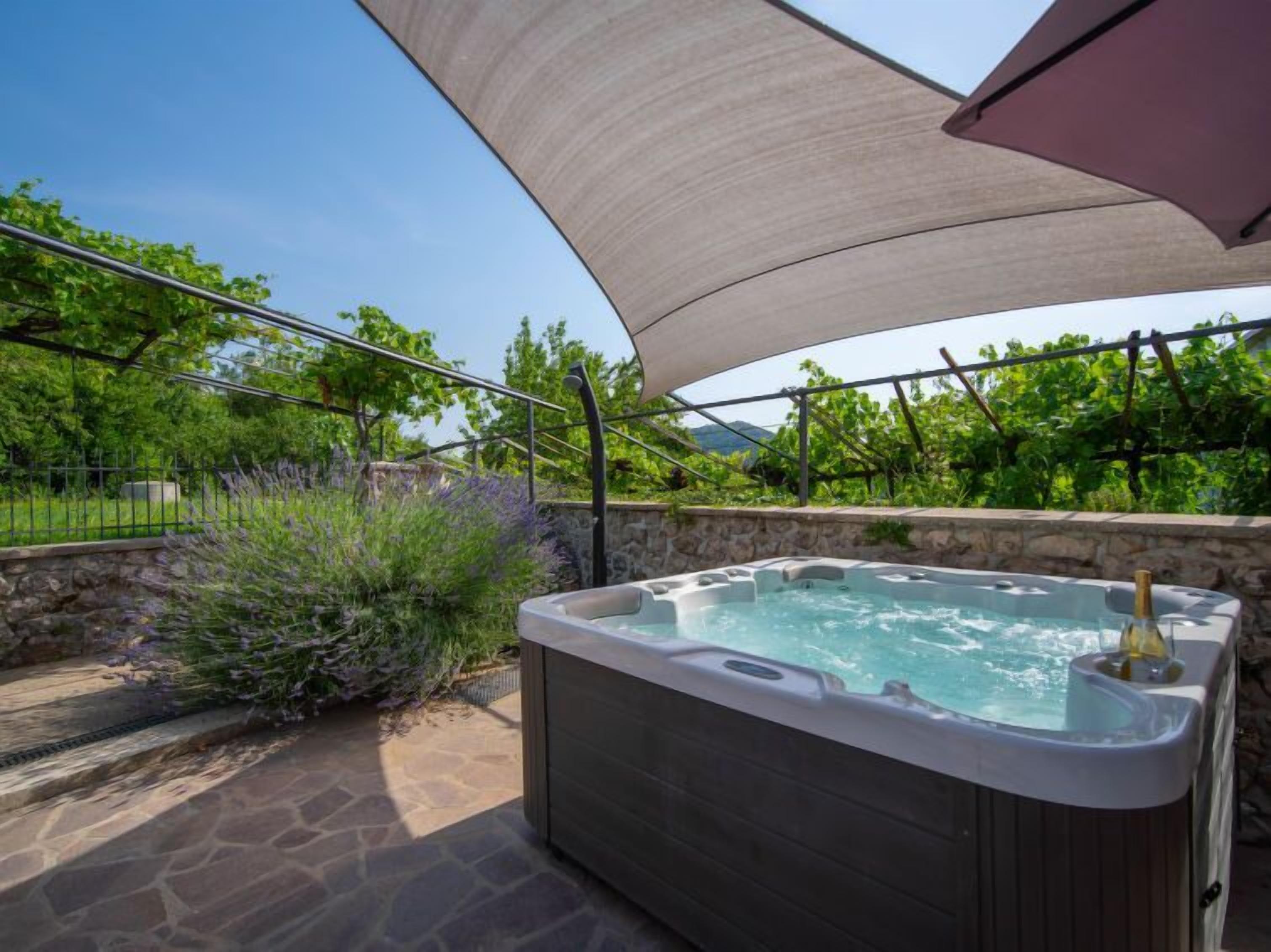 Een hottub in een tuin met een stenen muur en begroeiing.