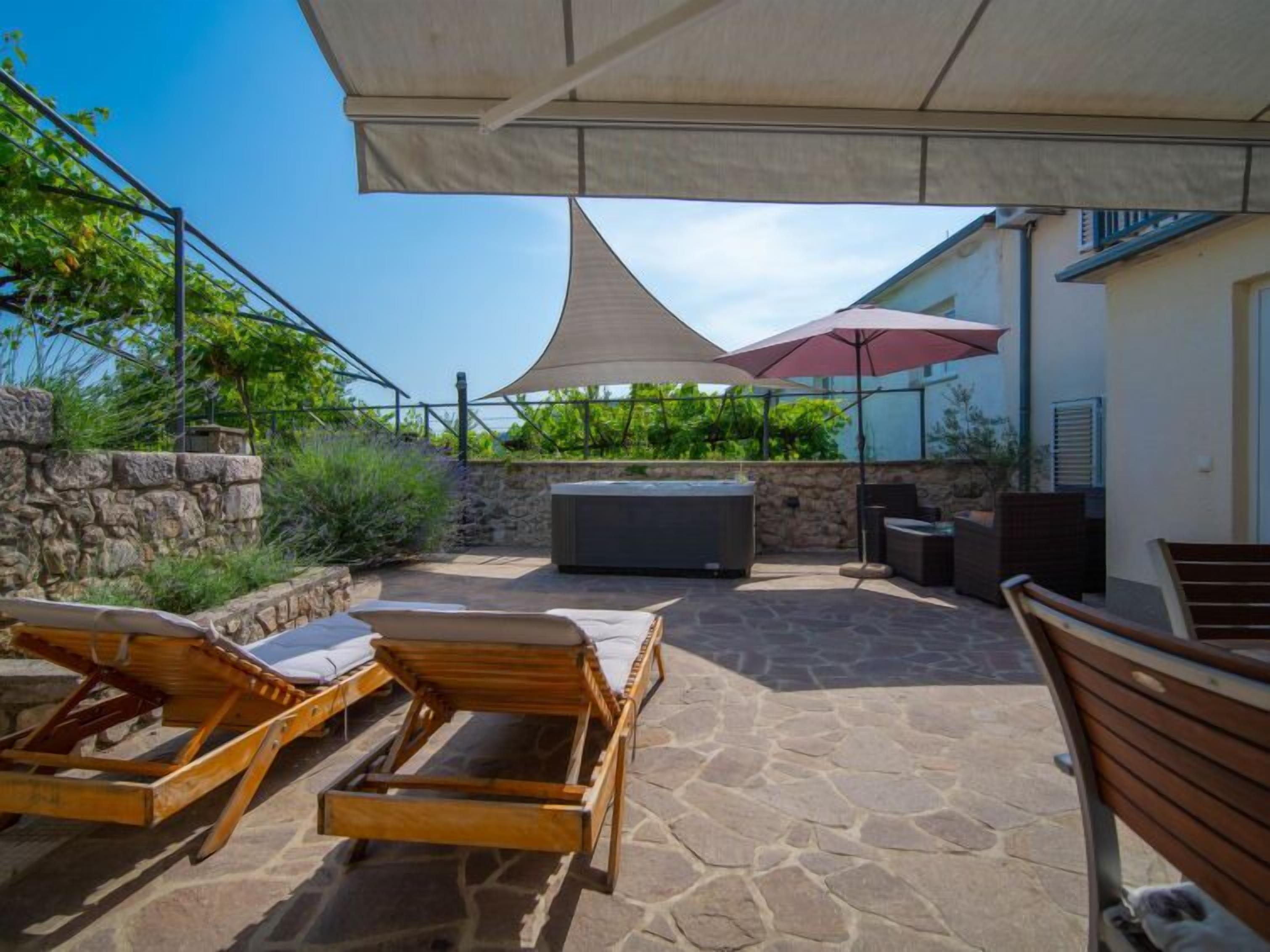 Un patio exterior con sillones de descanso, una bañera de hidromasaje y una zona de barbacoa.