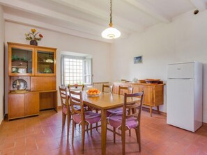 A dining area with a wooden table and chairs, a cabinet with glass doors, a white refrigerator, and a window with a view of the outside.