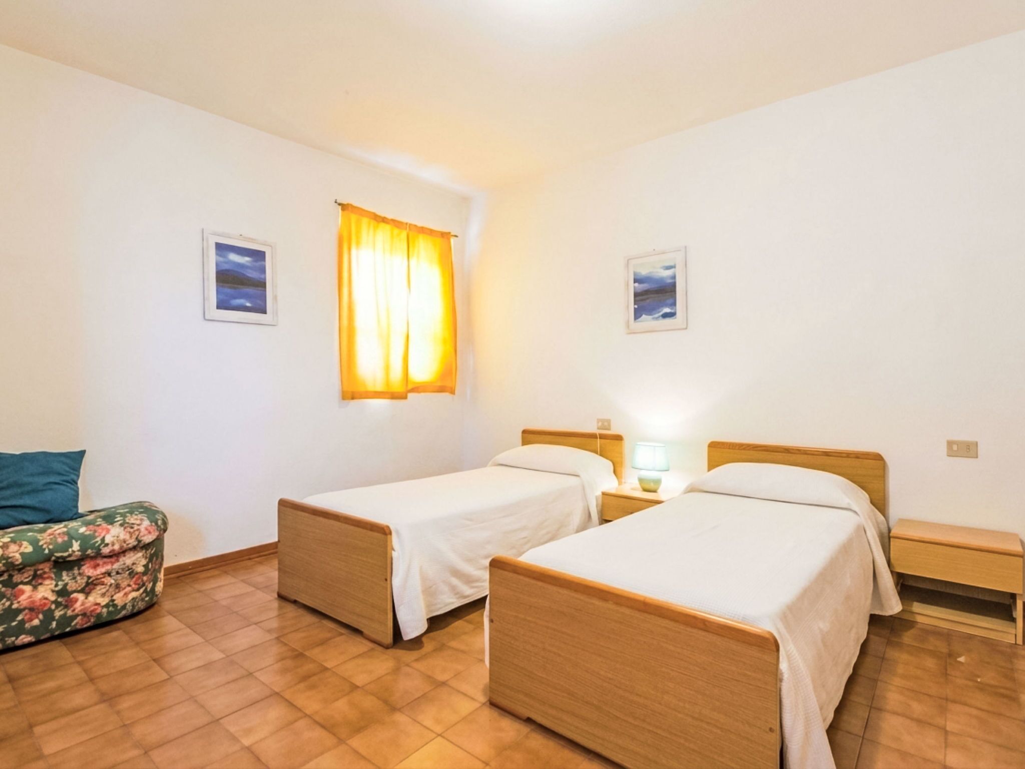 Una habitación con dos camas individuales, un pequeño sofá, una mesita de noche con lámpara y una ventana con cortinas.