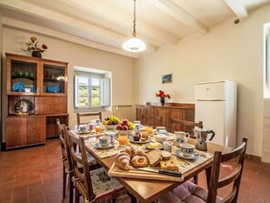 A dining area with a wooden table set for breakfast, including croissants, bread, and fruit.