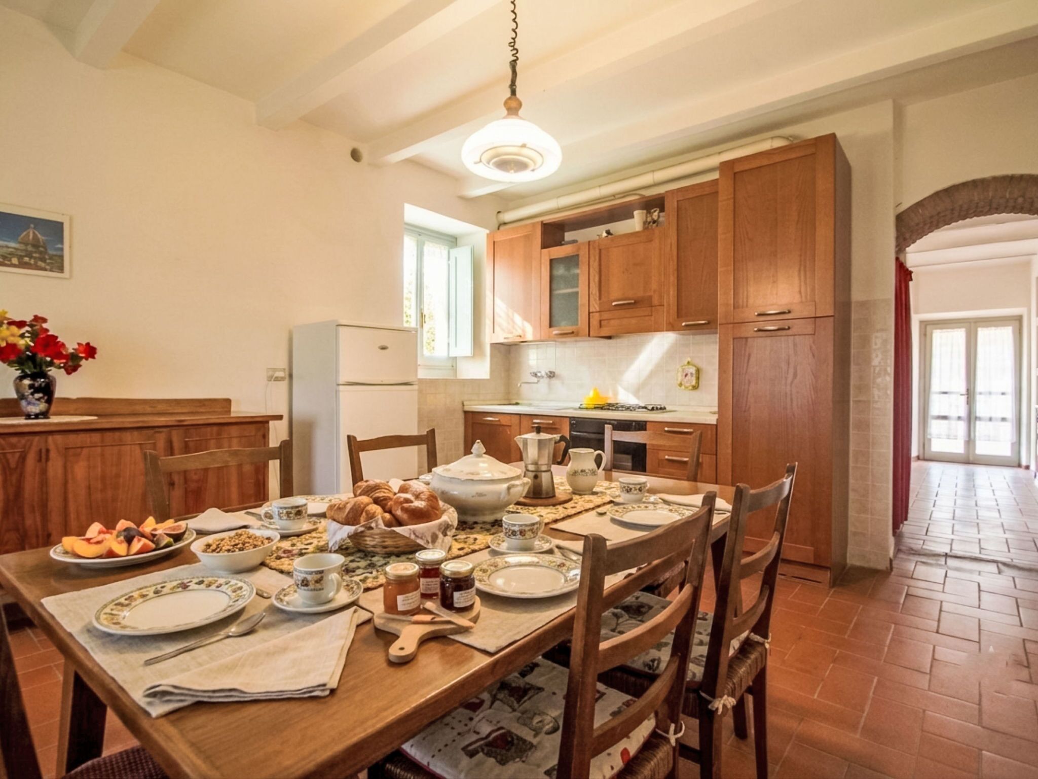 A dining area with a wooden table set for breakfast, including croissants, bread, and various breakfast items.