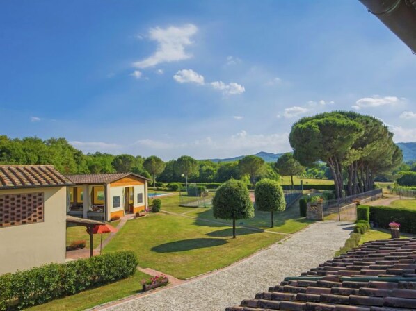 Eine Villa mit gepflasterter Auffahrt, Rasen und Tennisplatz.