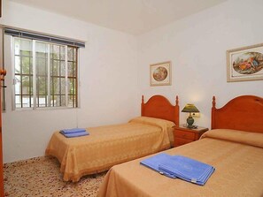 Een slaapkamer met twee eenpersoonsbedden, een raam met tralies, een klein nachtkastje met een lamp en twee ingelijste foto's aan de muur.