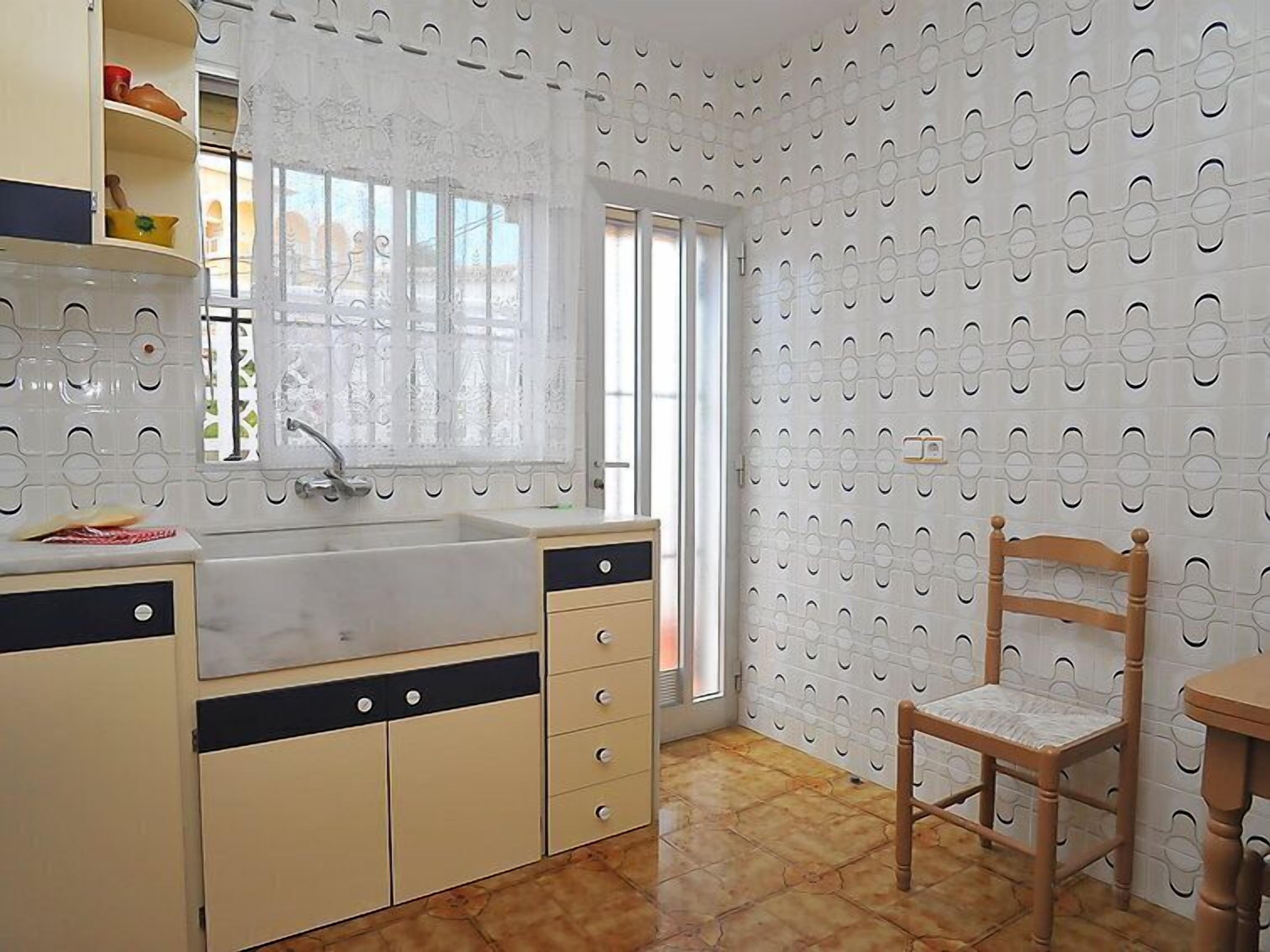 A kitchen with a sink, cabinets, and a chair.