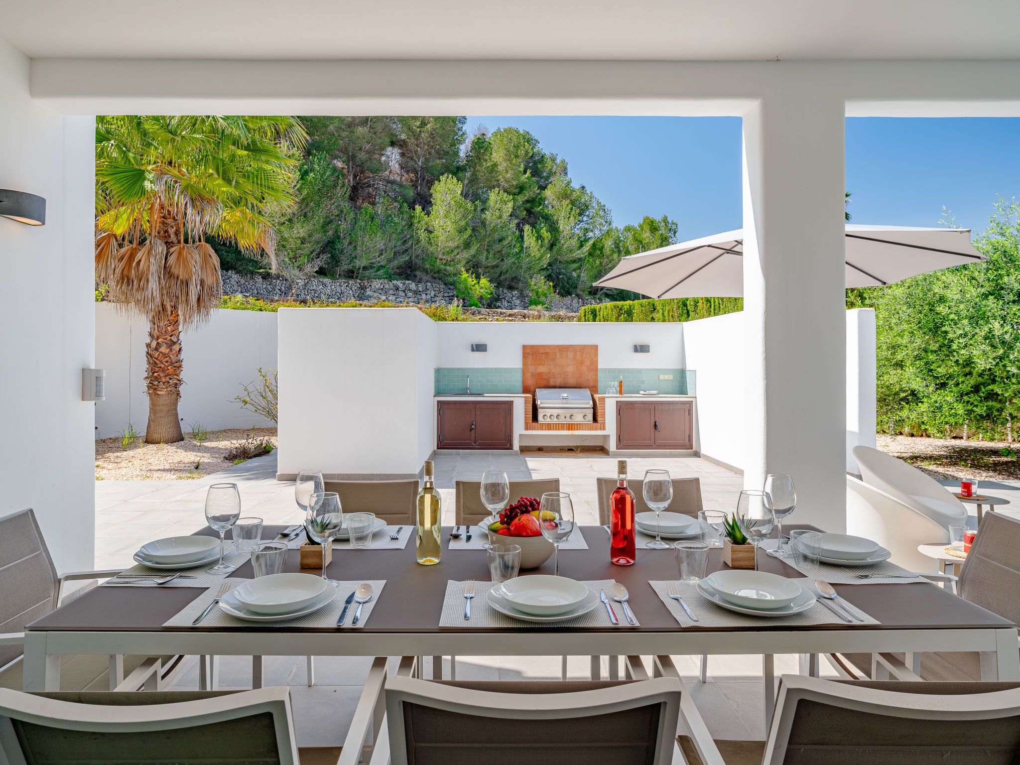 An outdoor dining area with a table set for six, a grill, and a view of a mountainous landscape.