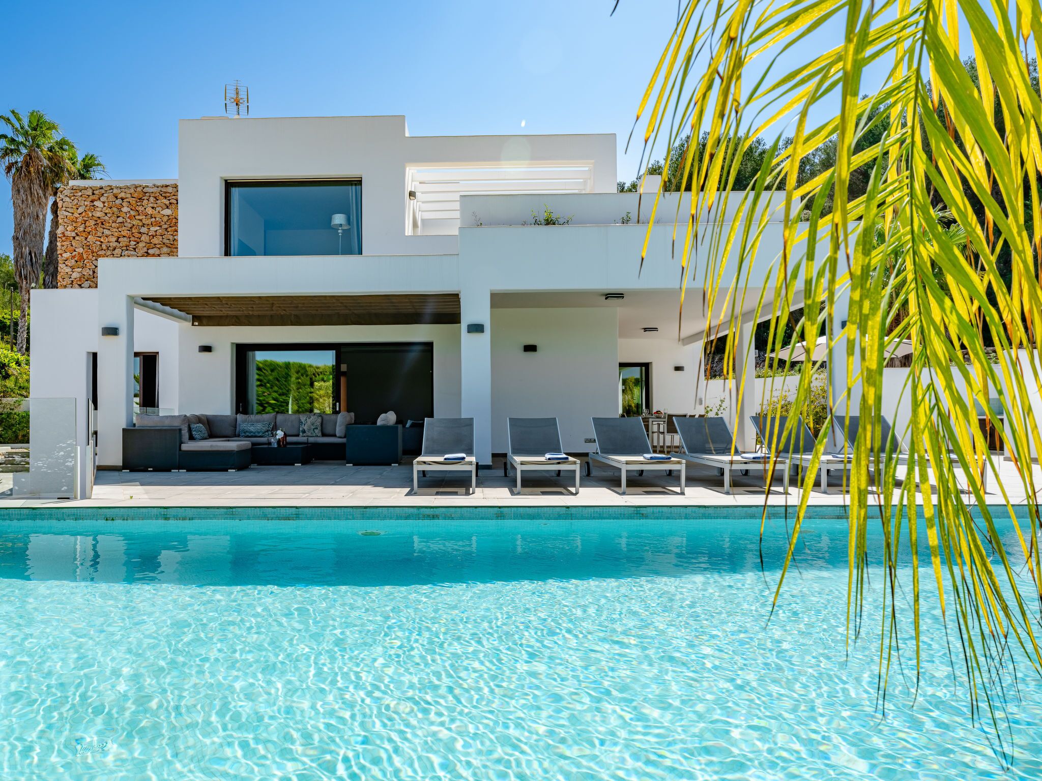 A modern house with a pool, outdoor seating, and a stone wall.