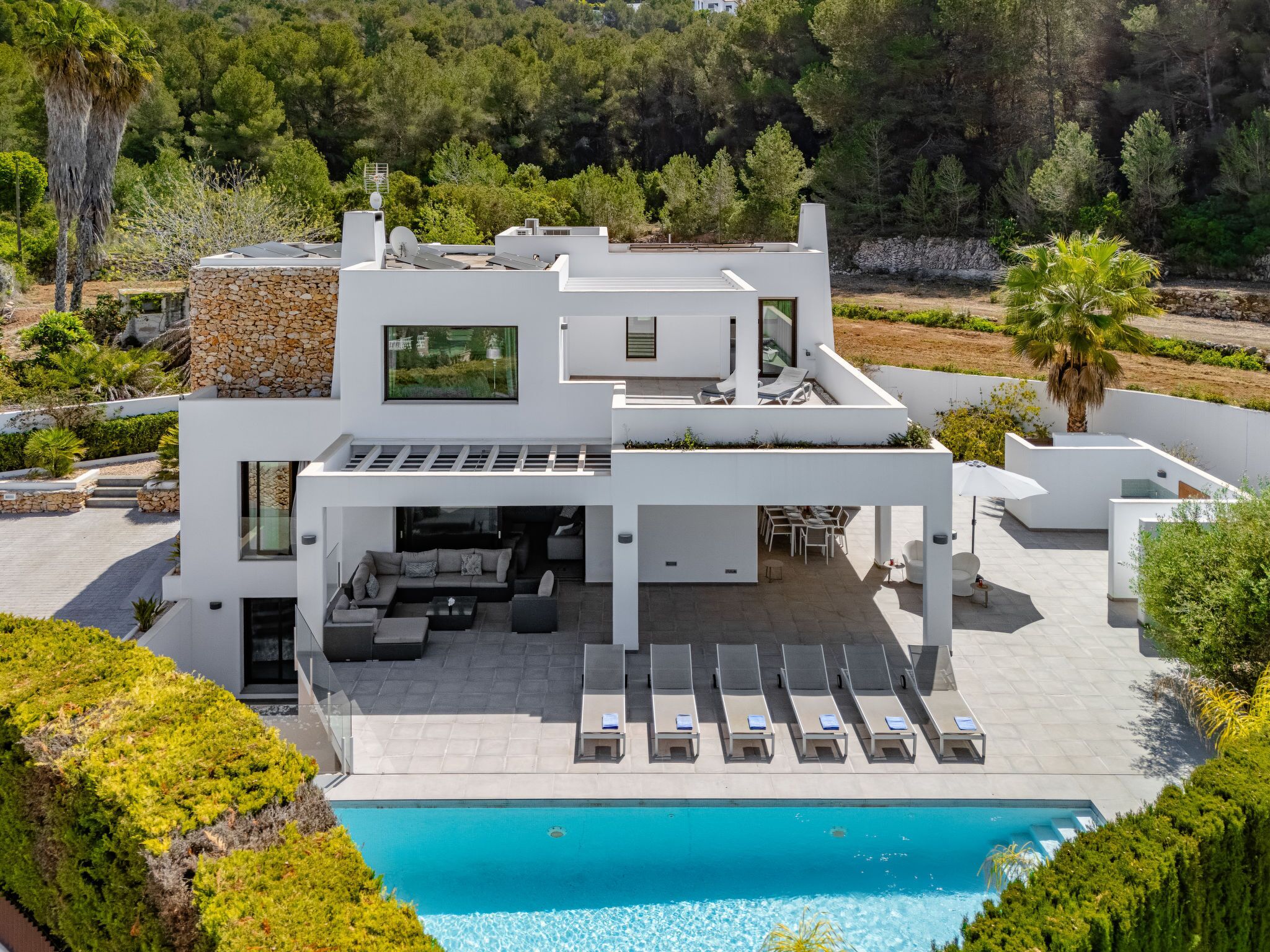 A modern two-story house with a pool, outdoor seating, and a view of the surrounding greenery.