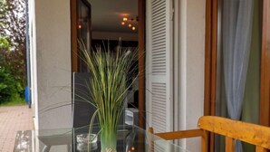 Una mesa con cubierta de vidrio, un florero con hierba verde, un vaso transparente y una silla de madera.