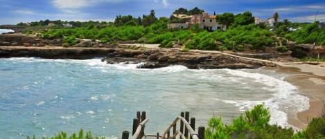 A coastal walkway leading to a beach with rocky outcrops and a view of a town in the distance.