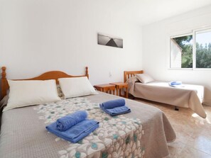 A bedroom with a large bed, a smaller bed, a desk, and a window.