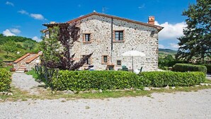 A stone building with a gravel driveway, a small patio with a table and chairs, and a white umbrella. - Agriturismo Antee by Interhome (Arcidosso)