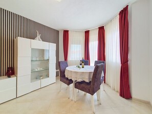 Un coin repas comprenant une table ronde, quatre chaises, un buffet aux portes vitrées et des rideaux rouges.