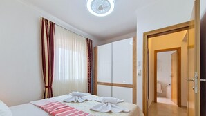 Ein Hotelzimmer mit zwei Betten, Holzboden, einer Tür zu einem Badezimmer und einem Deckenventilator.