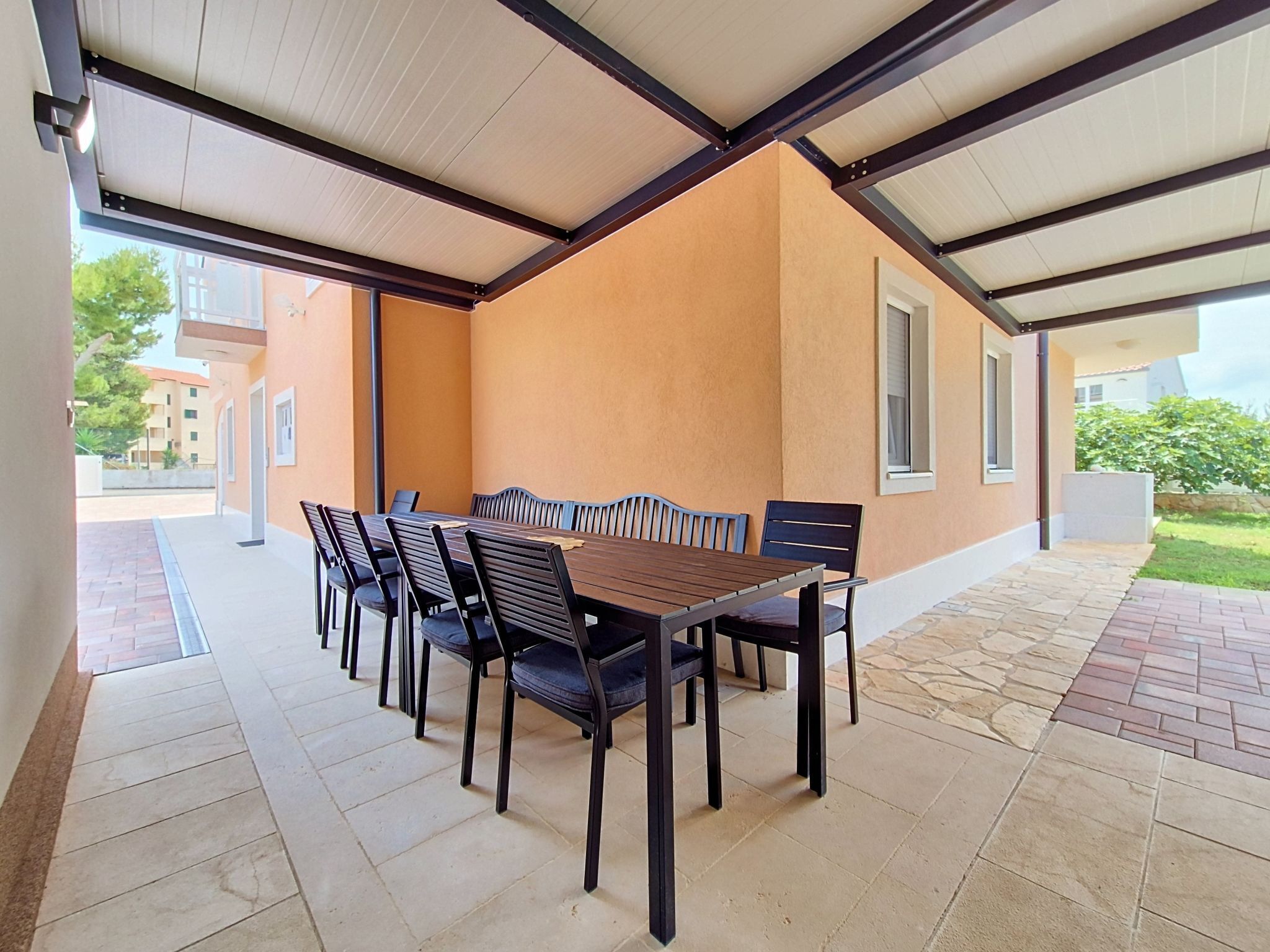 An outdoor patio with a wooden table and chairs, a covered roof, and a view of the surrounding buildings.