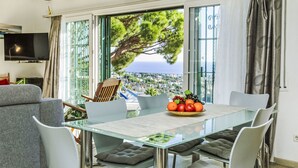 A modern living room with a glass dining table, grey sofa, and a TV mounted on the wall.