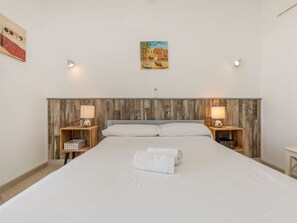 Ett hotellrum med en sänggavel i trä, en säng med vita sängkläder, två sängbord med lampor och en tavla på väggen.