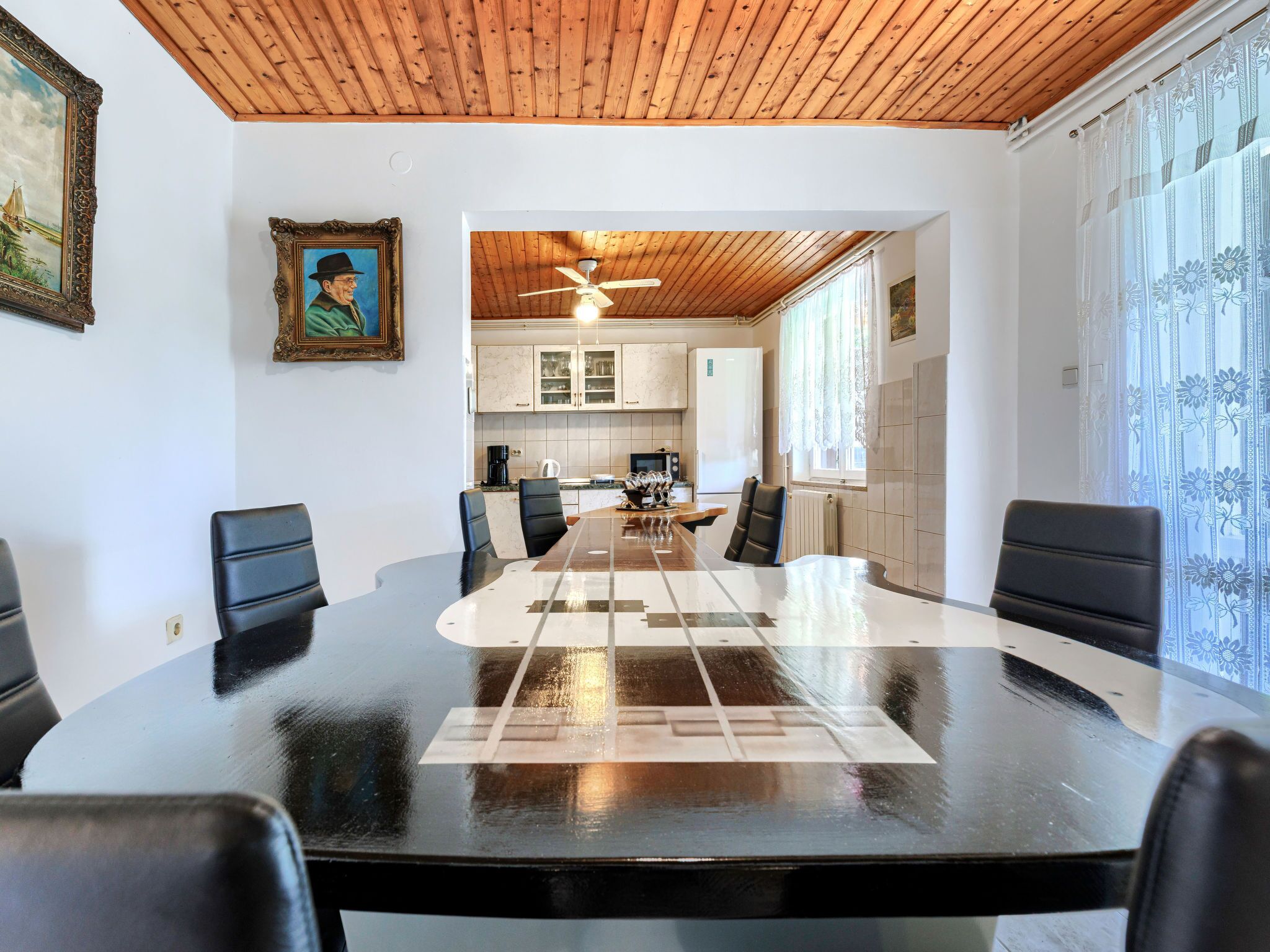 A conference room with a long table, black chairs, wooden ceiling, and a view into a kitchen area.