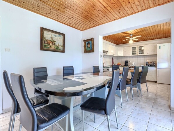 Un comedor con una mesa redonda y sillas, una cocina con armarios blancos y vigas de madera en el techo.