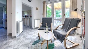 Un soggiorno con tavolo da pranzo, due poltrone, un termosifone e vista sulla cucina e sull'esterno.