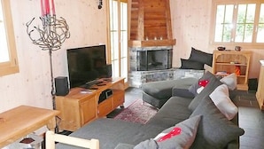 A cozy living room with a large grey sofa, a wooden TV stand, and a fireplace. - Chalet La Poya by Interhome (Moléson-sur-Gruyères)