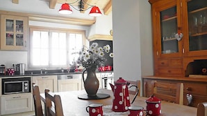 A kitchen with wooden cabinets, a dining table with red and white polka dot cups, a vase with white flowers, and a hanging light fixture. - Chalet La Poya by Interhome (Moléson-sur-Gruyères)