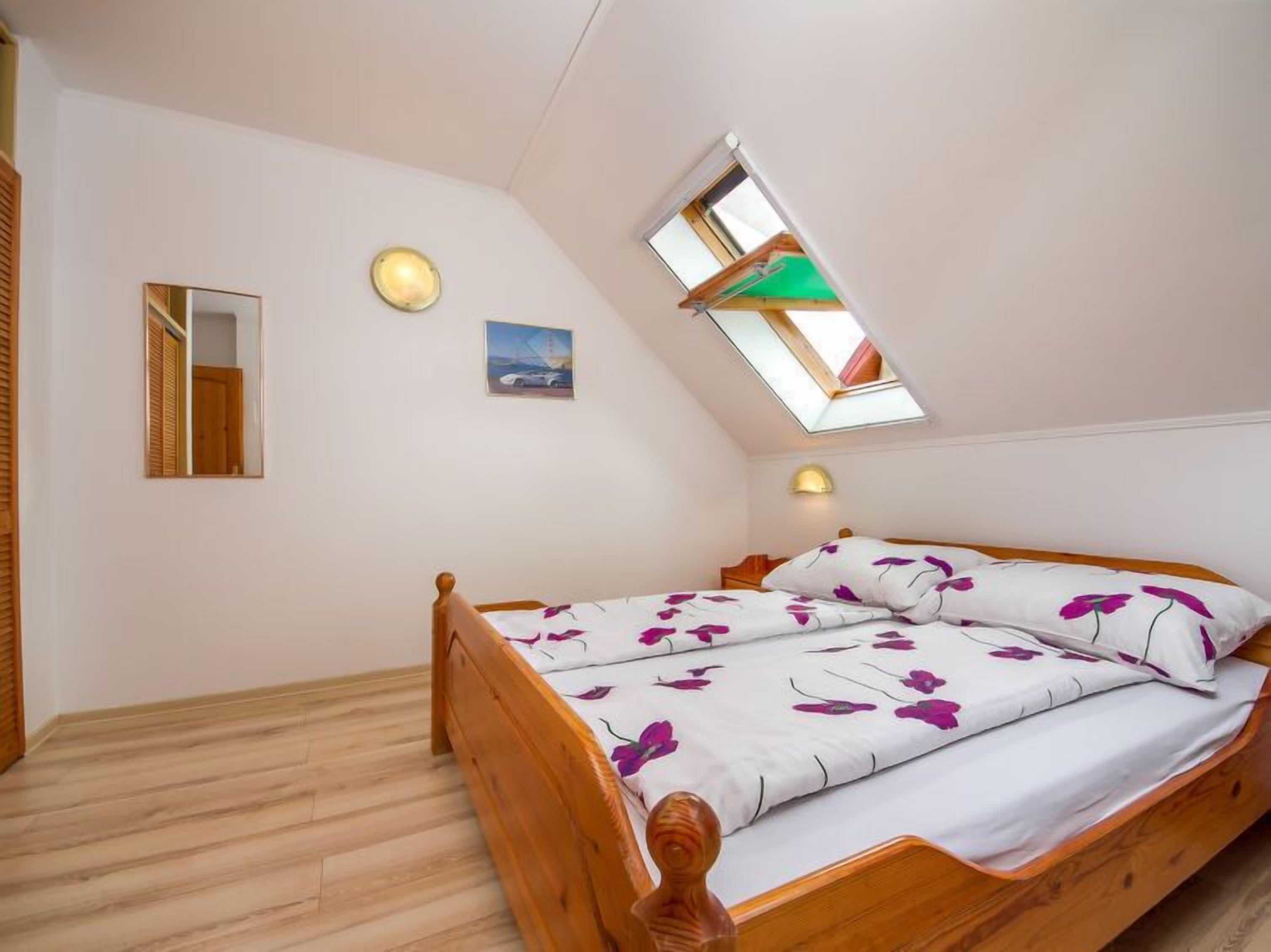 A bedroom with a sloped ceiling, a skylight, a bed with floral bedding, a bedside lamp, and a framed picture on the wall.