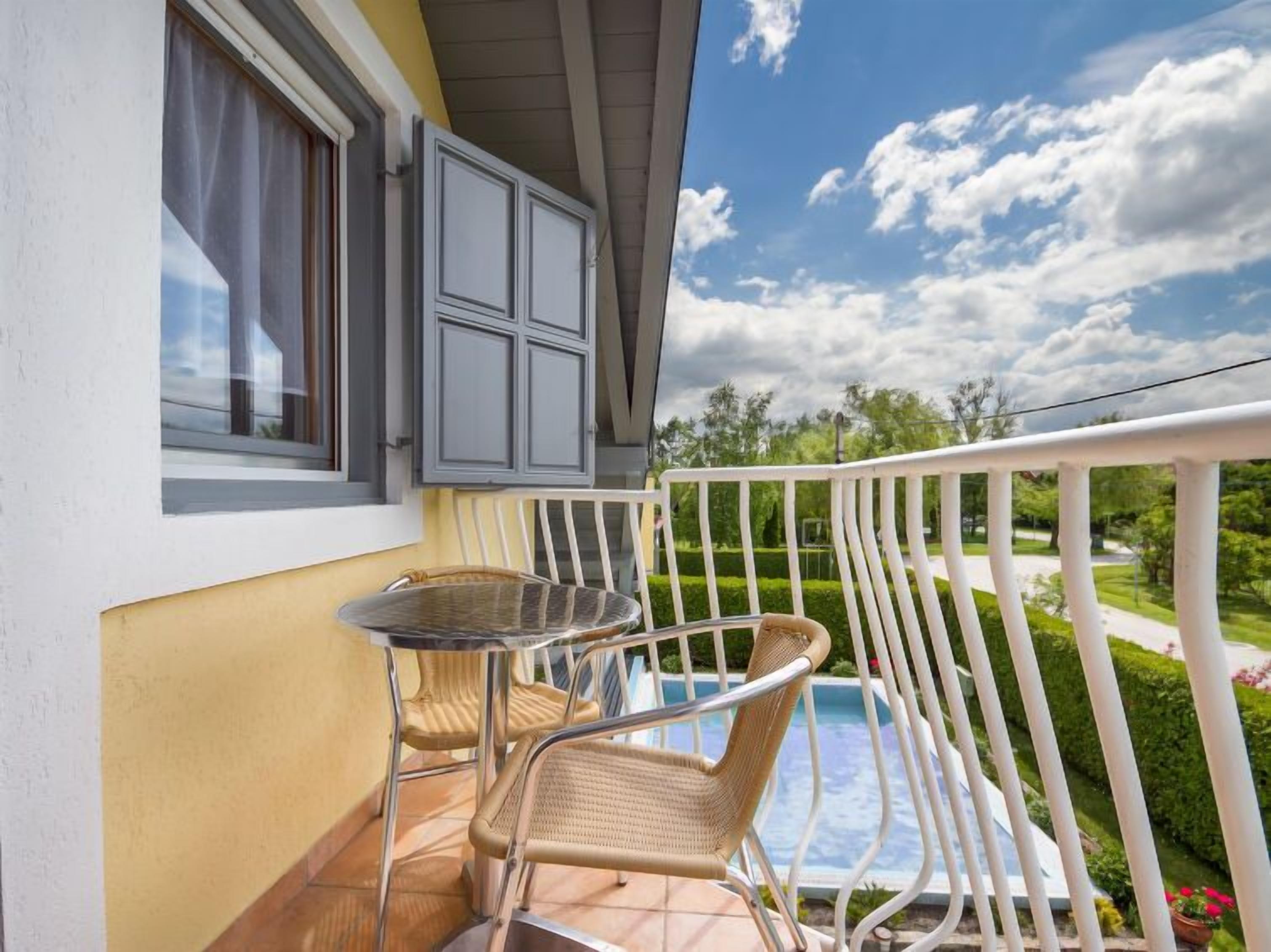 Un balcón con mesa y sillas, vista a una piscina y un jardín.