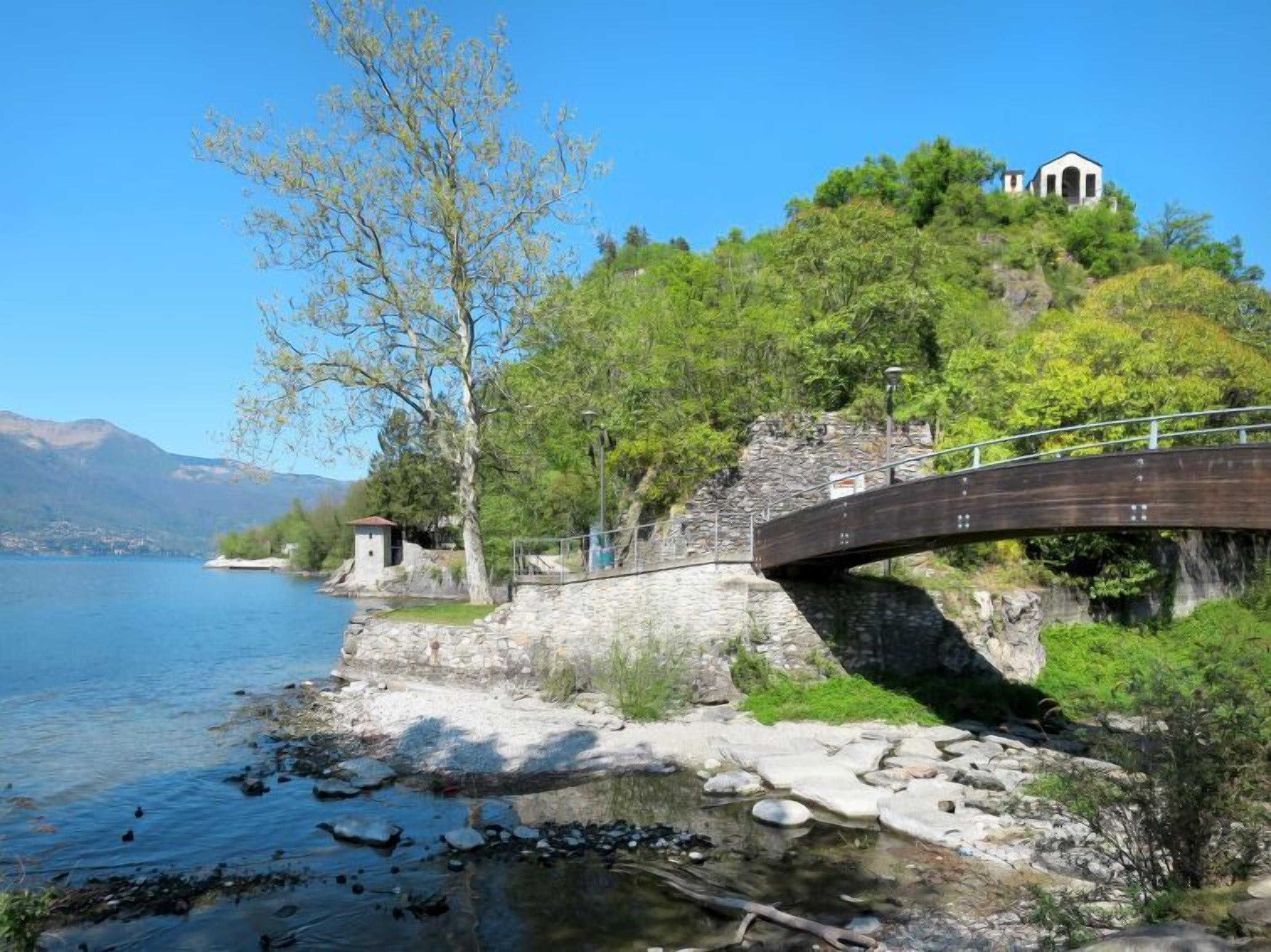 Un puente de piedra sobre un lago tranquilo, un pequeño edificio en una colina y abundante vegetación.
