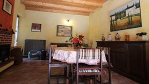 Un comedor con techo de madera, una mesa con mantel floral y sillas. Hay un cuadro en la pared y un jarrón con flores sobre la mesa.