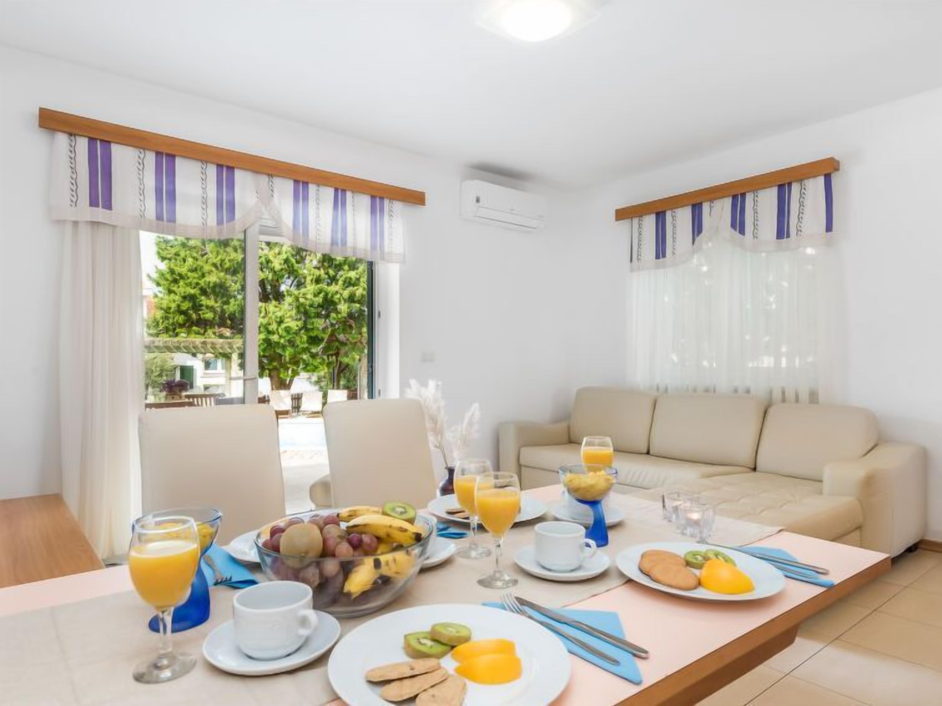 A breakfast setup with a table, chairs, a sofa, and a view of greenery outside.