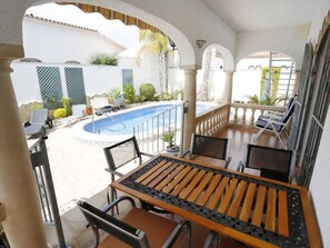 Zona junto a la piscina con mesa y sillas, una piscina y vistas al jardín circundante.