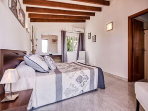 Une chambre à coucher avec un lit, une table de chevet, une lampe, des poutres en bois au plafond et une porte.