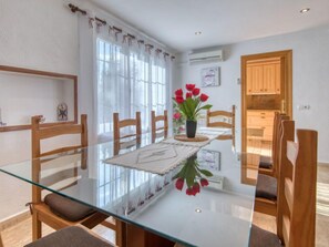 Un coin repas avec une table en verre, des chaises en bois et un vase rempli de fleurs rouges.