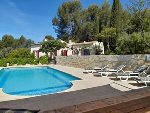 A swimming pool with lounge chairs, surrounded by stone walls and trees.